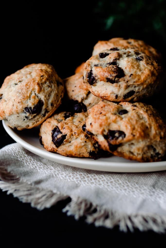 sourdough scones with chocolate chips and coconut stacked on a cream colored plate on a cream colored woven towel