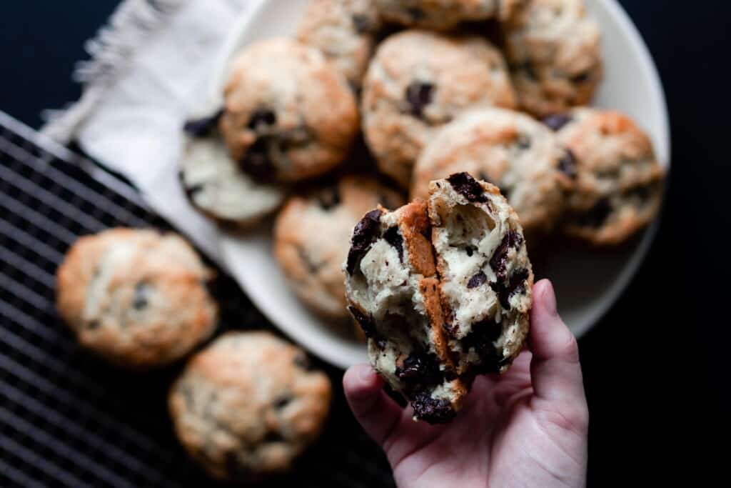 hand holding a sourdough scone broken in half with a plate full of scones behind it