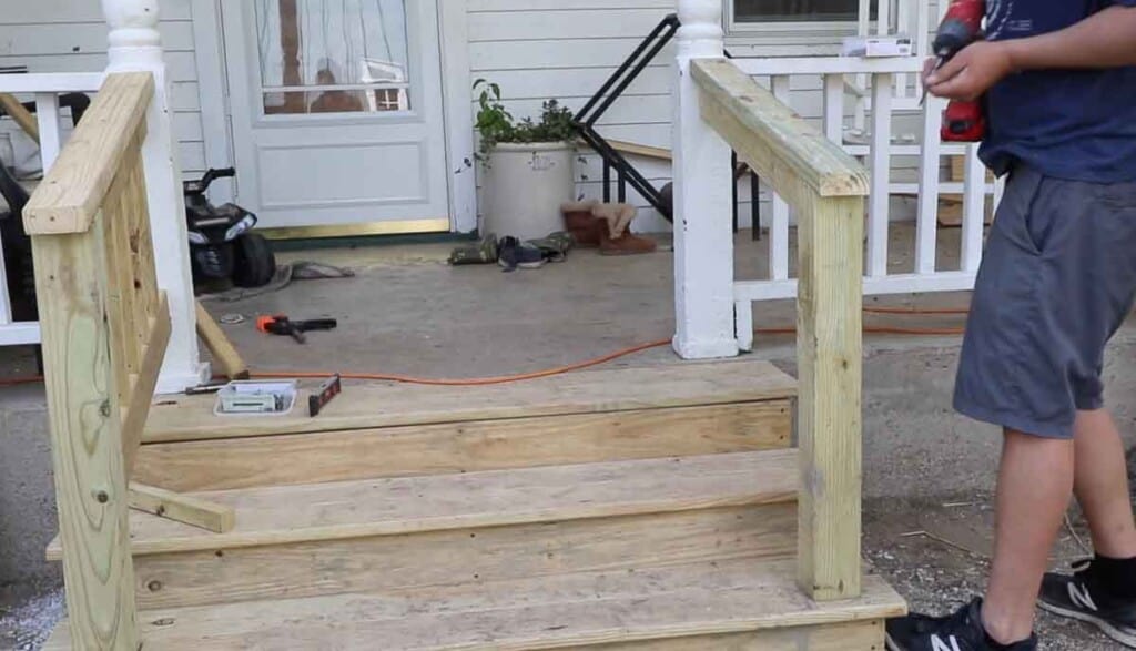 man adding a 2 by four to the top of a front porch step hand rail to finish it off.