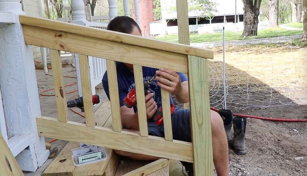 man drilling spindles into a hand rail of front porch steps to match the spindles on the front porch.