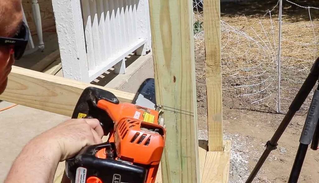 man using a chainsaw to cut off the top of a post to create a hand rail on front porch stairs