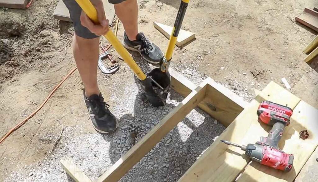 Man using a post hold digger to dig out a hole right next to stair stringers to add a post.