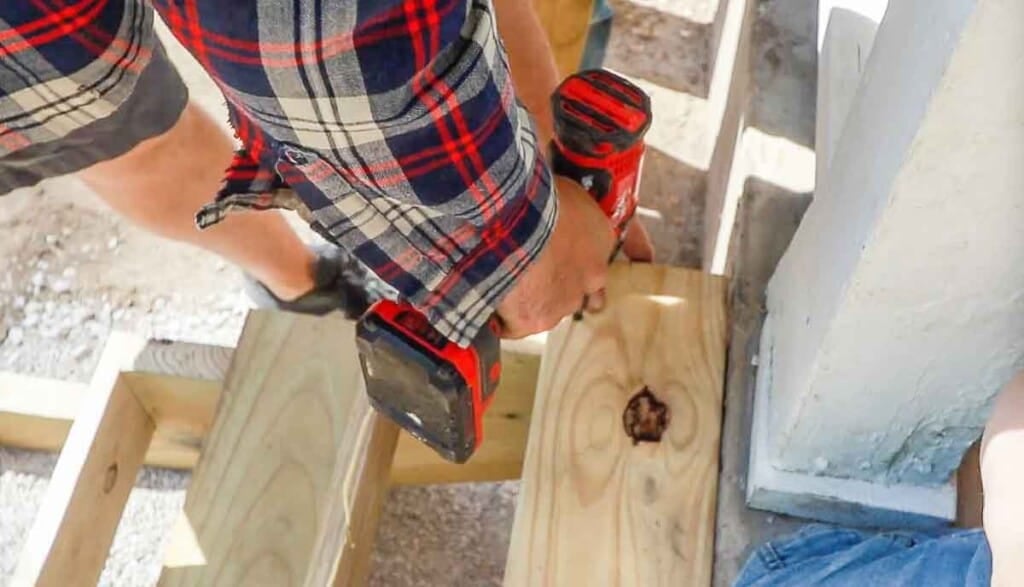 Man drilling stair treads into a stair stringers on a front porch