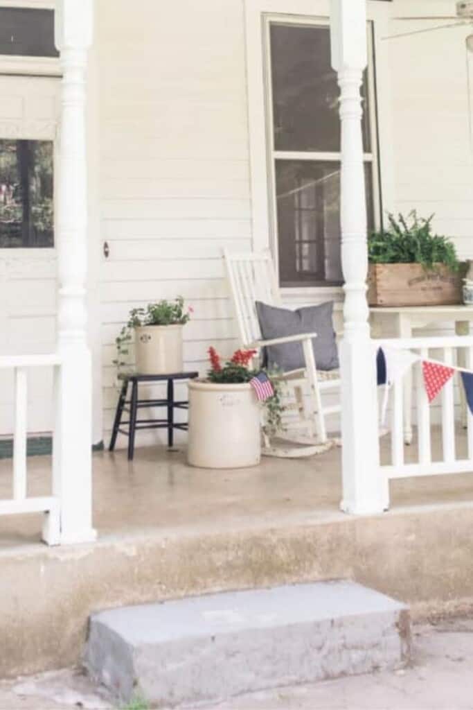 before picture of a a white victorian farmhouse front porch with a concrete step. Vintage pots with flowers and a rocking chair sit on a the porch