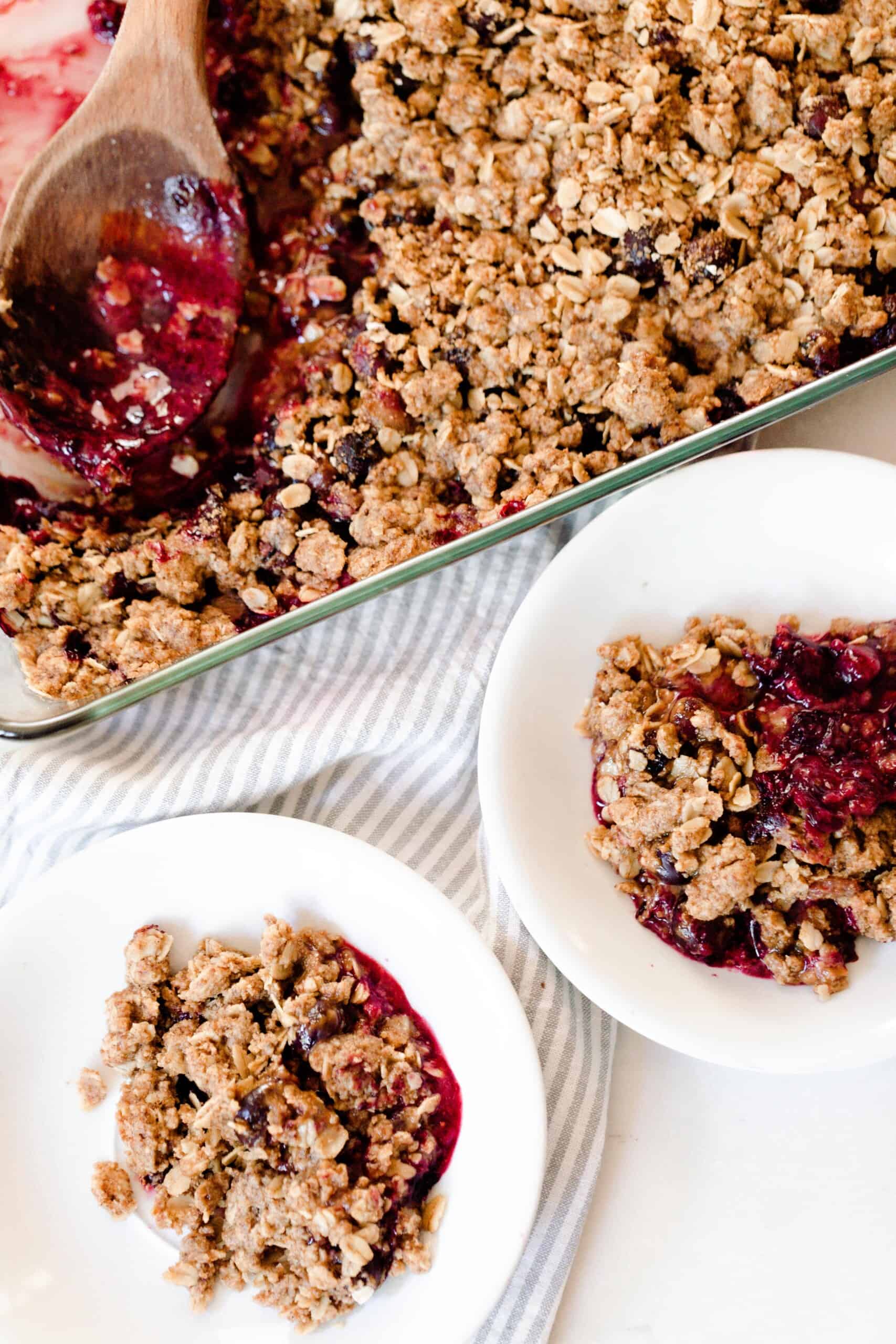 overhead photo of two white bowls filled with einkorn berry crisp with a baking dish of crisp behind the bowls in a background