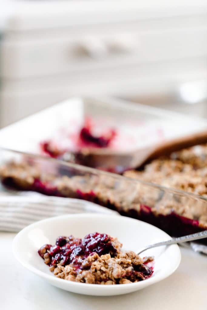 einkorn berry crisp in a white bowl with a spoon and more crisp in a glass baking dish in the background