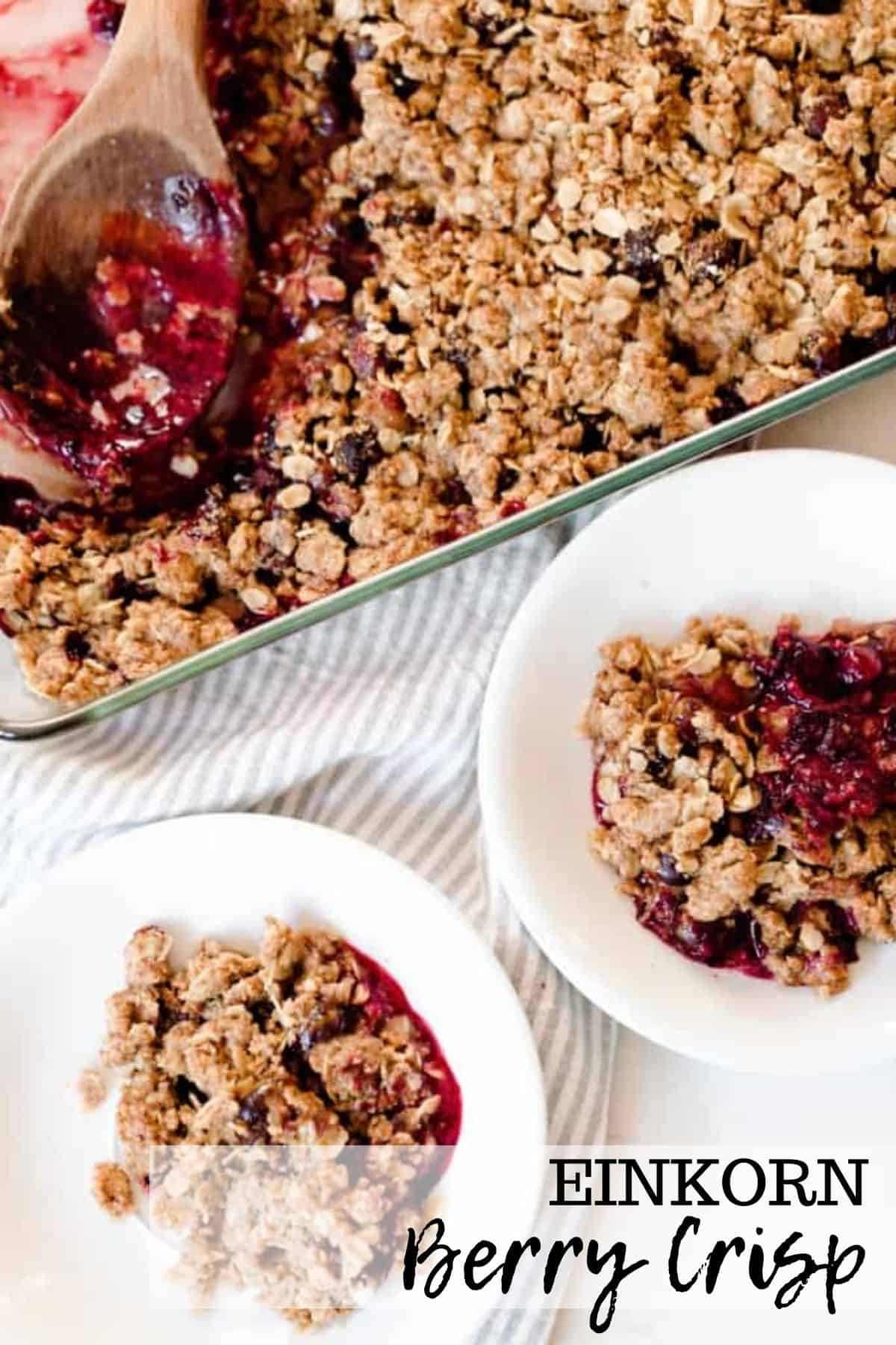 overhead photo of two white bowls filled with einkorn berry crisp with a baking dish of crisp behind the bowls in a background