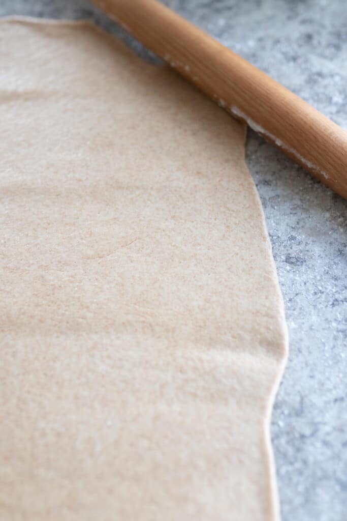 sourdough roll dough rolled out on a countertop with a rolling pin toward the back