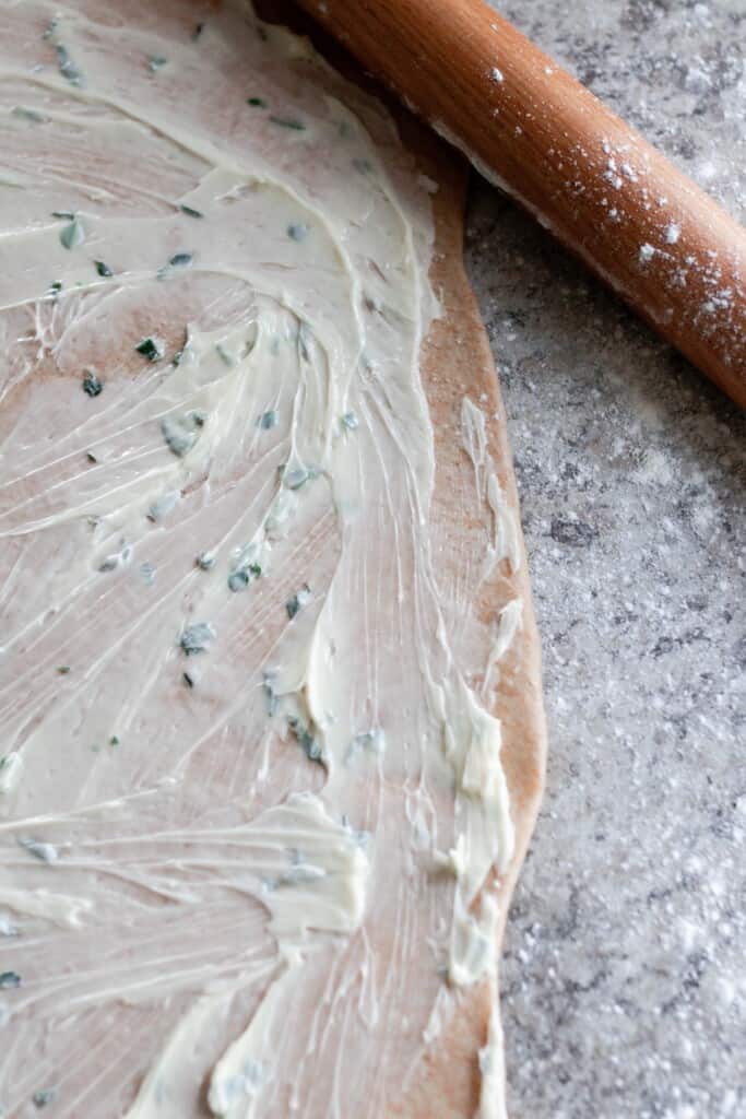 herb butter spread out on sourdough roll dough