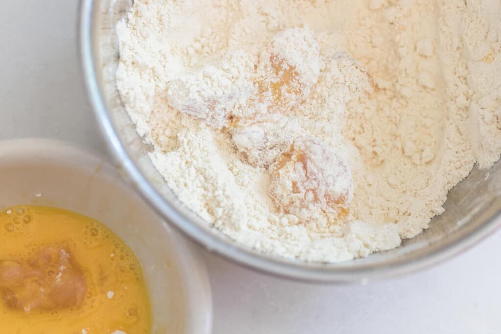 chicken pieces being dipped into einkorn flour bowl with another bowl of whisked eggs to the left