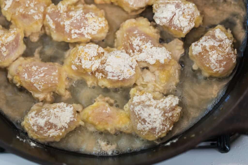 cut up chicken with in a einkorn flour coating being fried I a cast iron skillet with oil