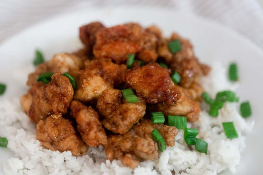crispy orange chicken with an einkorn coating on top of white rice with sliced green onion sprinkled on top