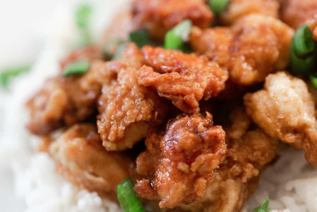 close up picture of homemade orange chicken made with einkorn flour with green onions on a bed of white rice