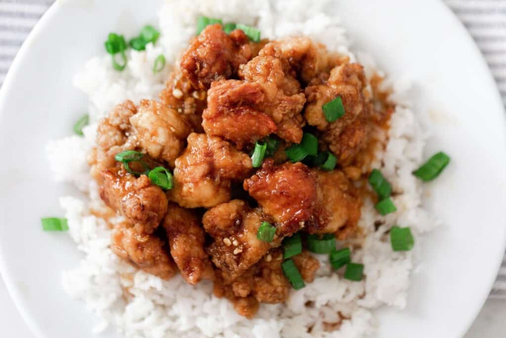 homemade orange chicken with an einkorn coating on a bed of white rice topped with sliced green onions sprinkled on top.