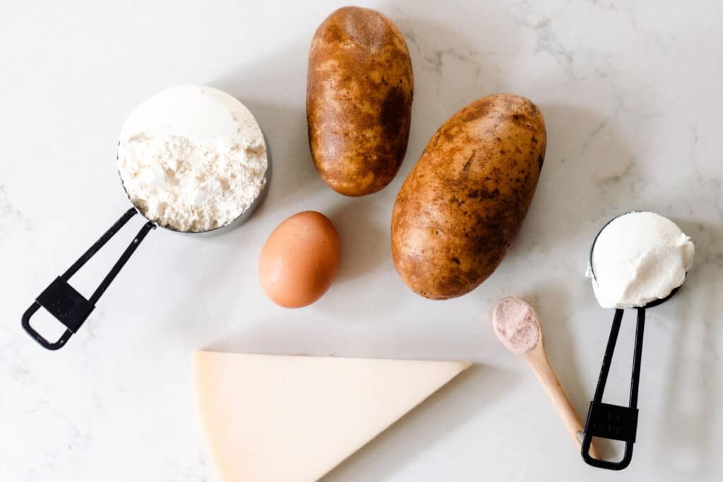 potato, einkorn flour, ricotta, egg, and a wedge of fresh parmesan cheese on a white quarts countertop