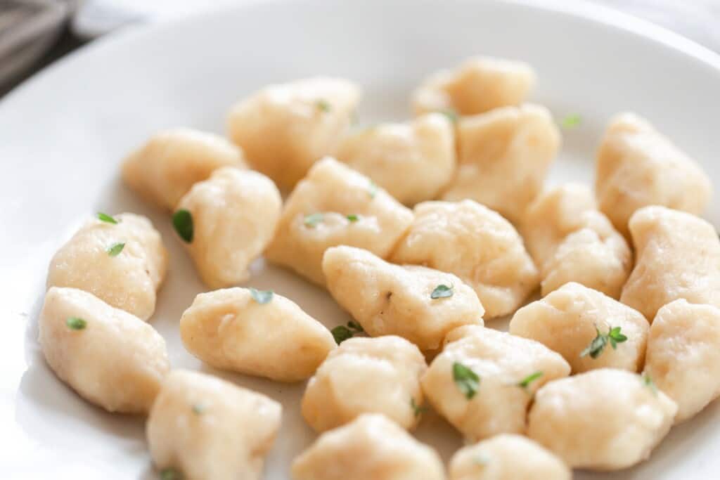 homemade gnocchi topped with herbs in a white bowl