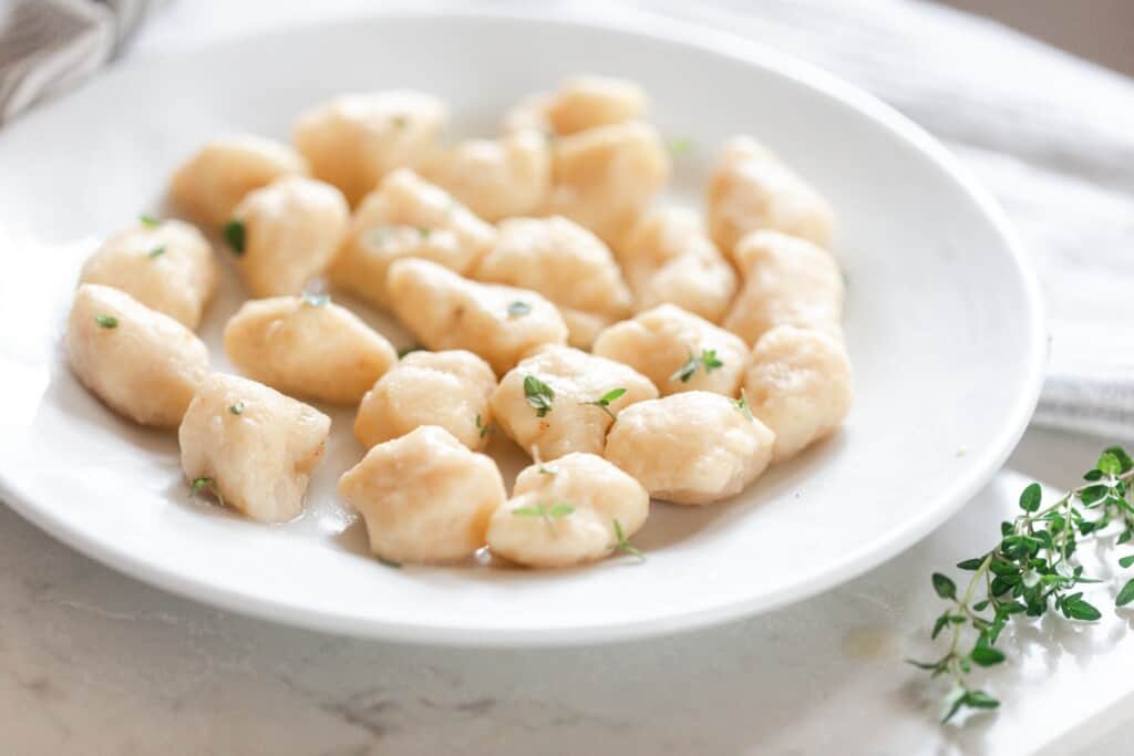 homemade einkorn gnocchi in a white bowl, topped with herbs, on a white quartz countertop with fresh thyme to the right