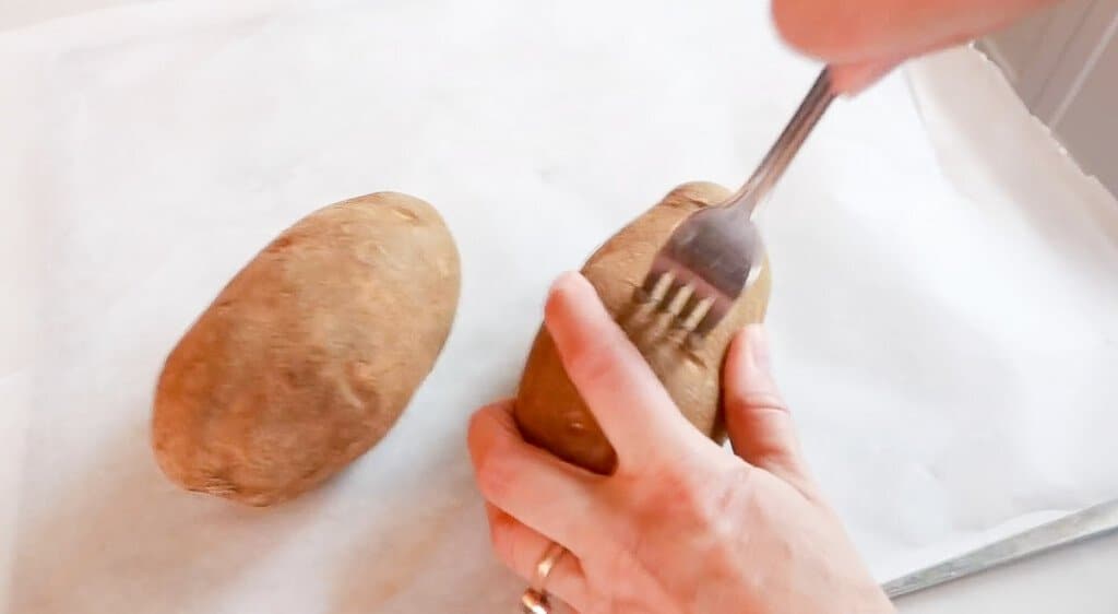 hand poking a potato with a fork so that it doesn't explode while baking