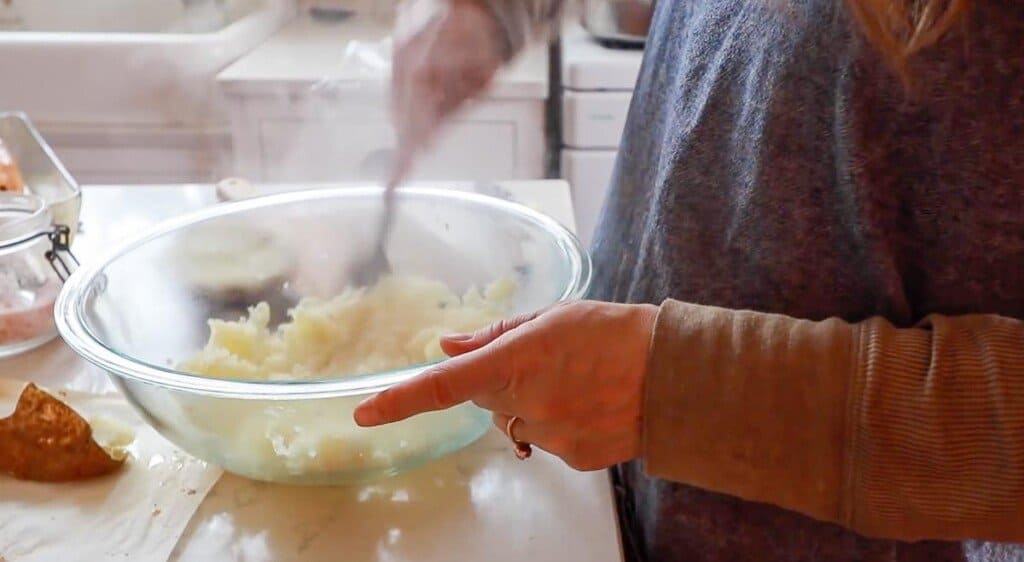 women wearing a blue pinafore apron mashing baked potatoes with a fork.