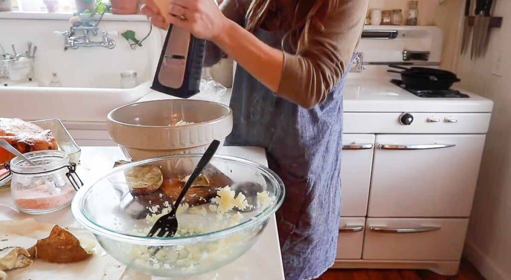 women wearing a blue pinafore apron grating fresh parmesan cheese into a bowl