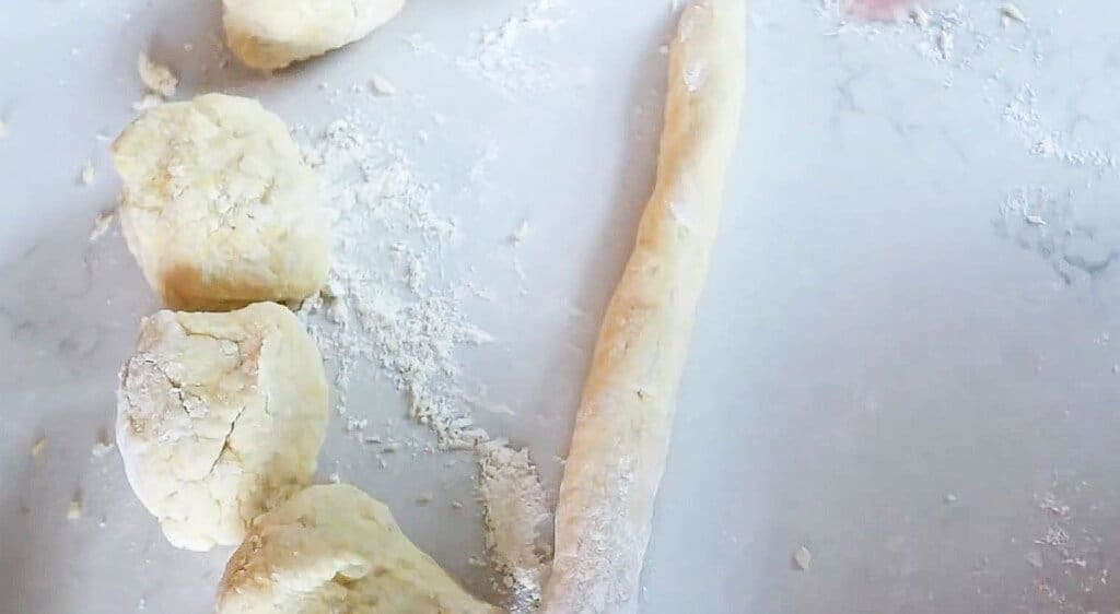 homemade gnocchi dough in 4 dough balls on a white counter top.  More dough is rolled into a long cylinder.