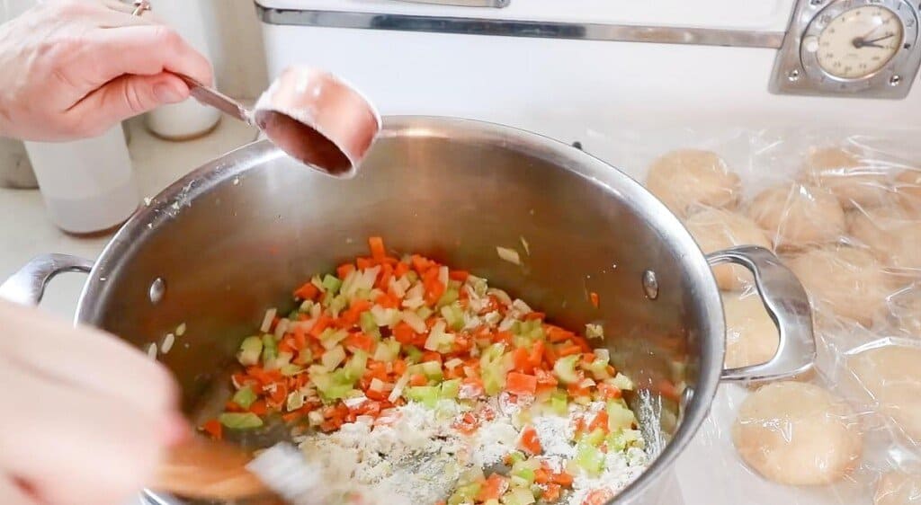 einkorn flour being added to diced veggies and butter in a pot to create a roux 