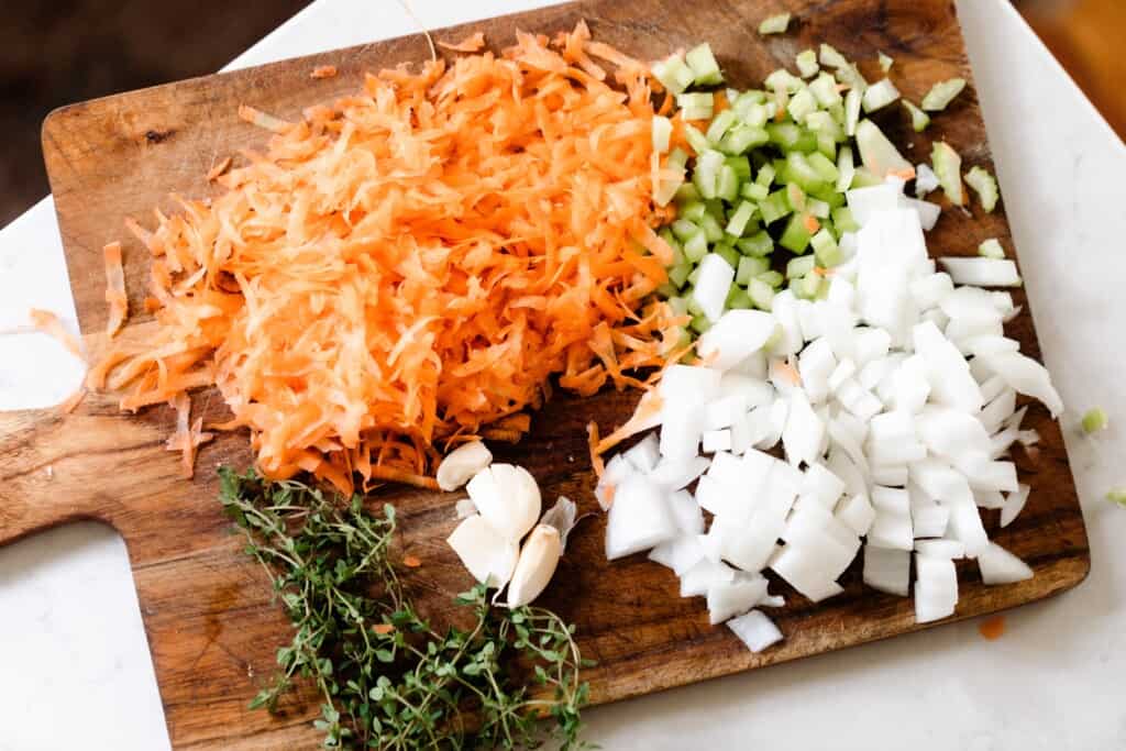 a cutting board filled with chopped onion, celery, carrots, whole garlic and fresh thyme