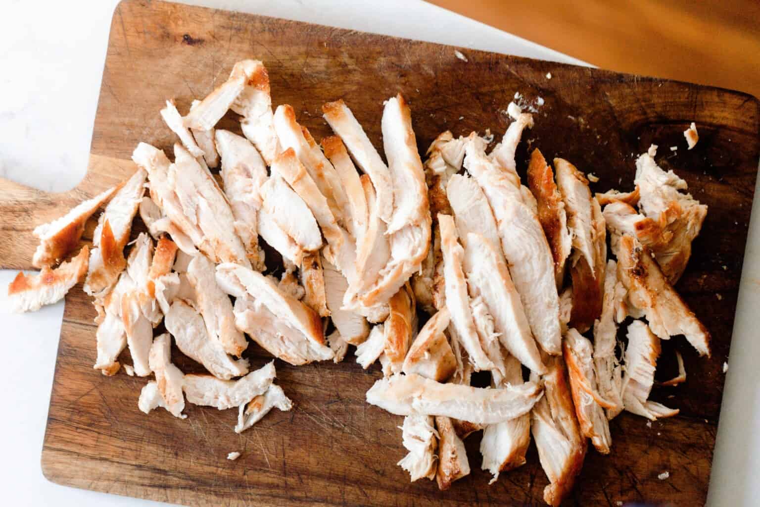 Pan fried chicken breast sliced on a wood cutting board.