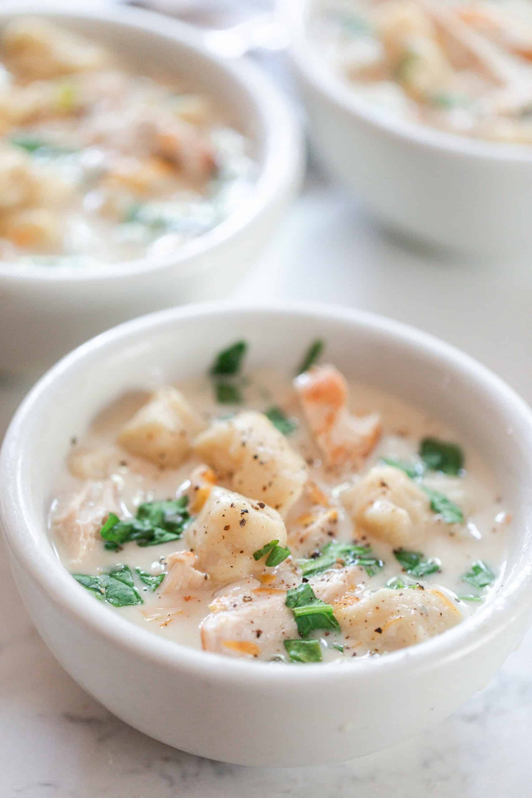three white bowls filled with homemade gnocchi soup topped with fresh herbs on a white and gray quarts countertop