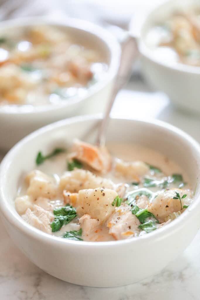 a bowl of creamy chicken and gnocchi soup in a white bowl with a spoon. More bowls of soup are in the background