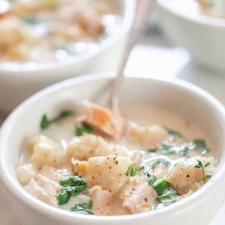 a bowl of creamy chicken and gnocchi soup in a white bowl with a spoon. More bowls of soup are in the background