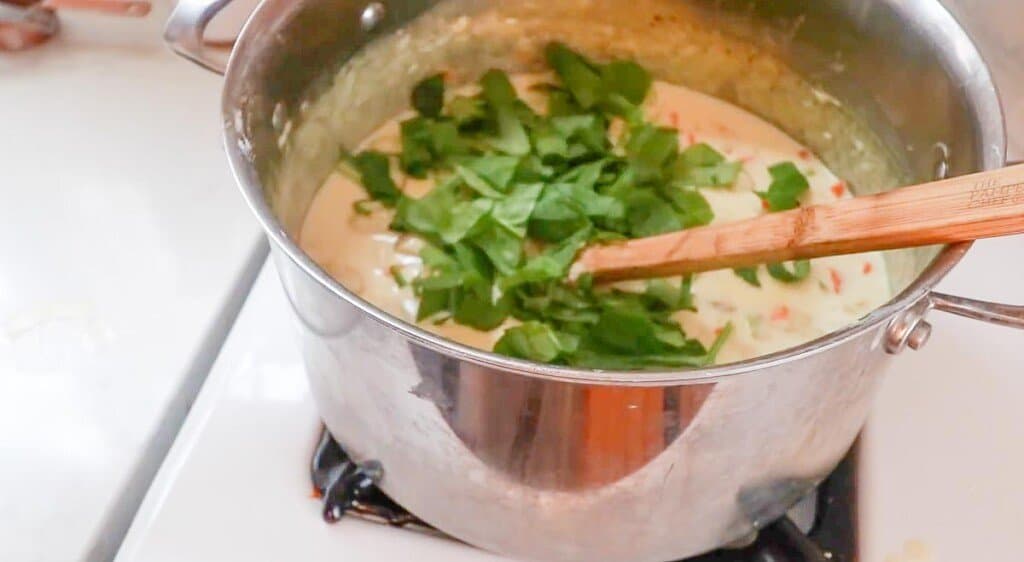 spinach added to a creamy gnocchi soup in a pot