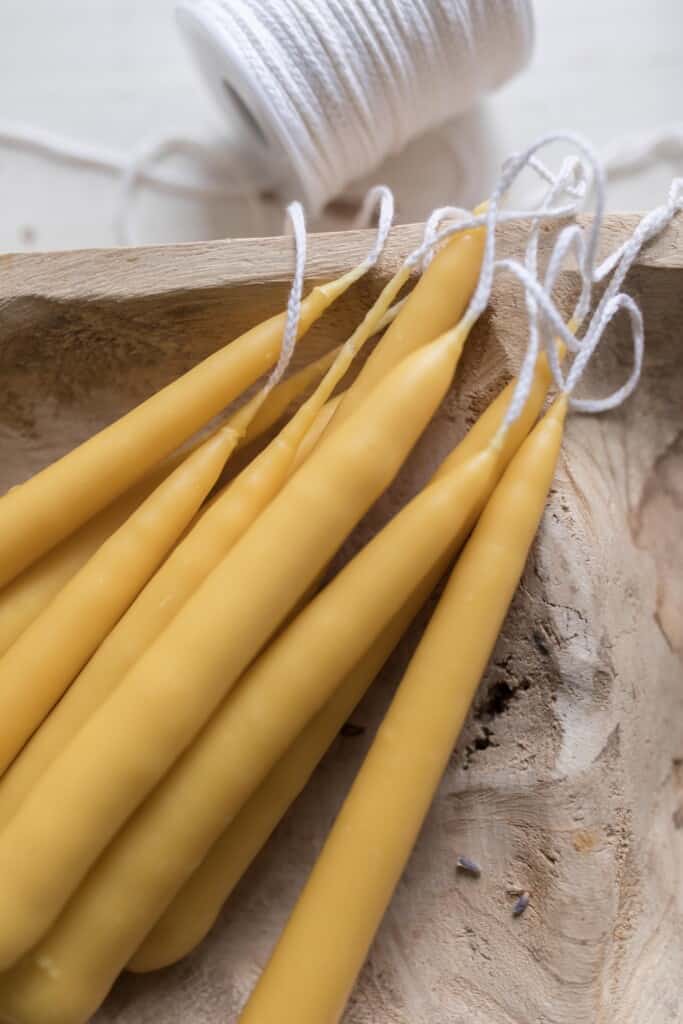 dipped beeswax tapered candles snacked on a wooden bowl with a spool of wick in the background