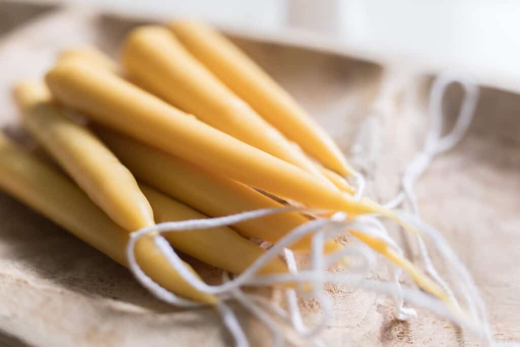 with beeswax tapered candles with white wicks in a hand carved wooden bowl