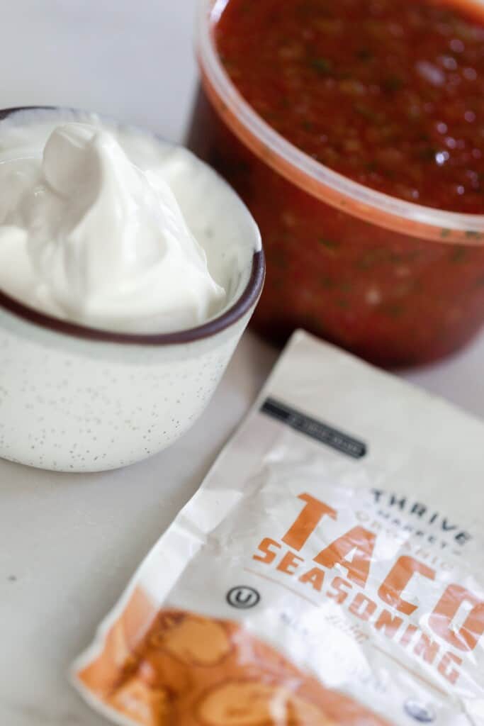 sour cream in a jar, red salsa in a container, and a packet of taco season