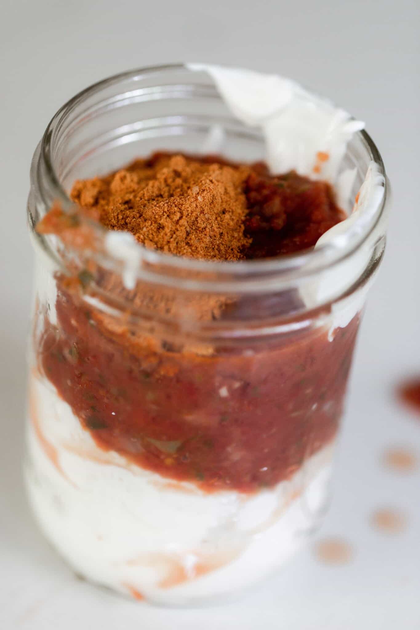 A mason jar filled with a layer of sour cream, salsa, and taco seasoning.