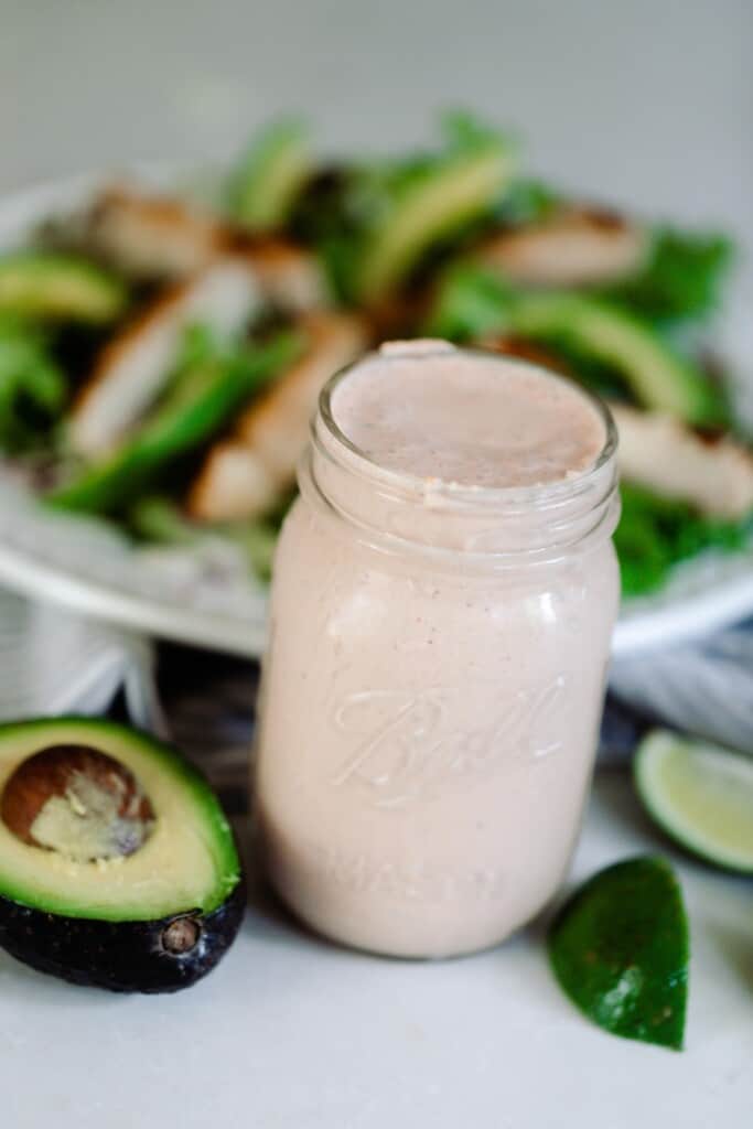 Mexican ranch salad dressing in a mason jar with a salad on a white plate in the background