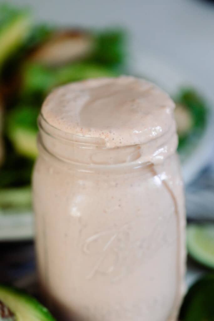 close up picture of taco ranch sauce in a mason jar with a salad on a plate in the background