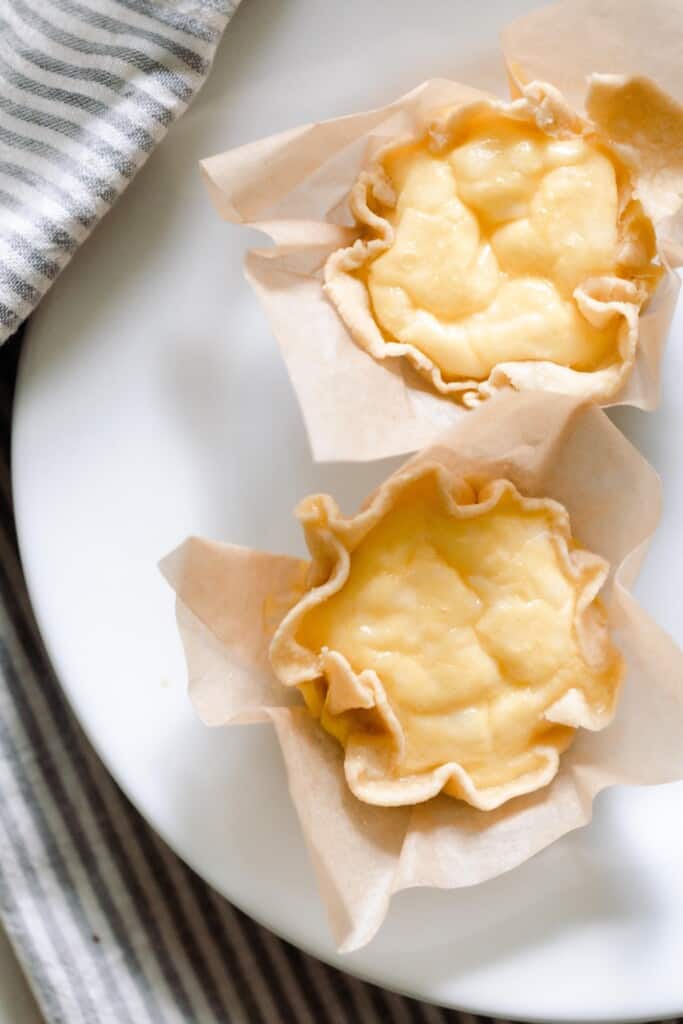 overhead photo of two mini quiches in parchment paper on a white plate with a gray and white stripped towel to the left