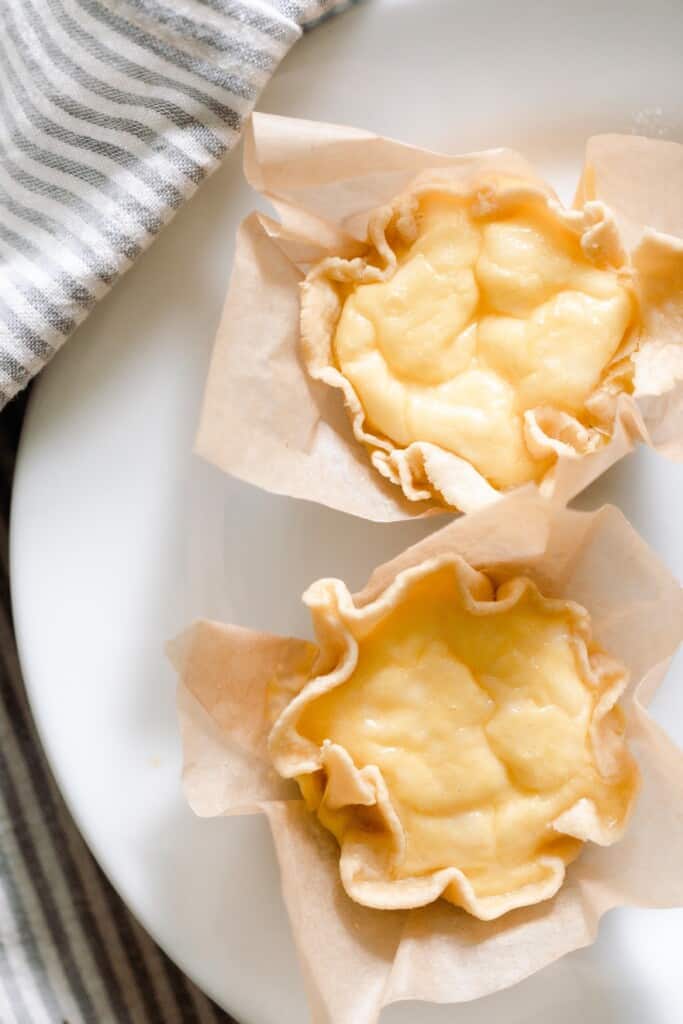 overhead photo of two mini quiches with a einkorn crust on a white plate with a gray and white towel to the left