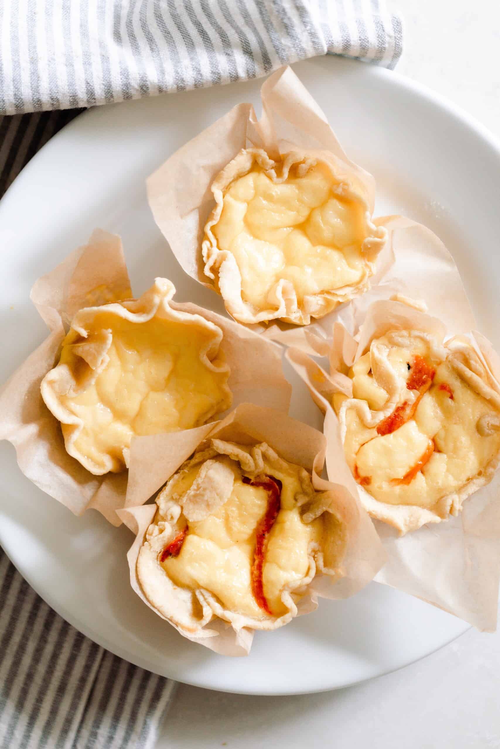 overhead photo of four mini quiches: two just plain with cheese, and two with roasted red pepper and onion) on a white plate