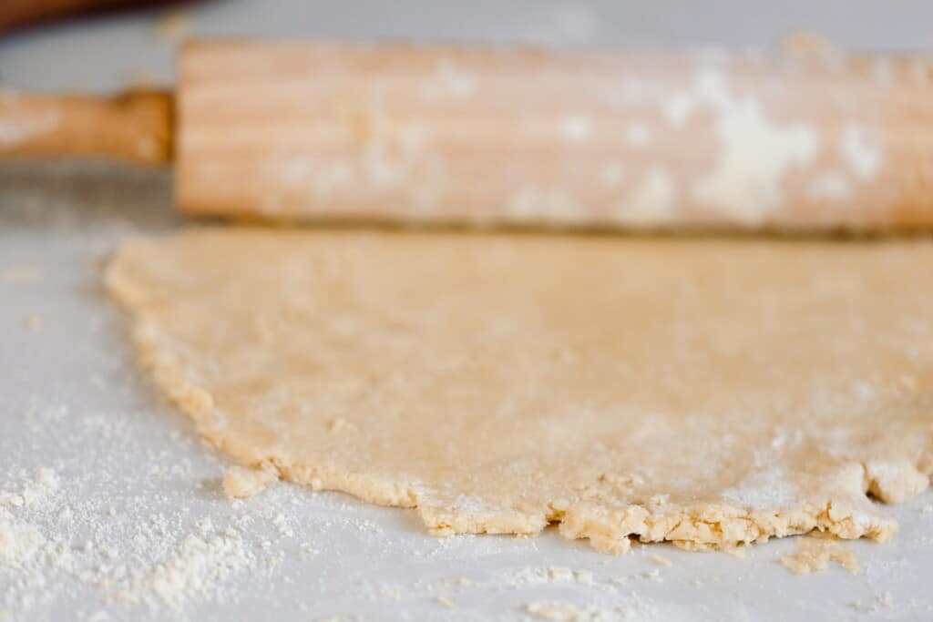 einkorn pie crust dough rolled out with a rolling pin on a white quarts countertop
