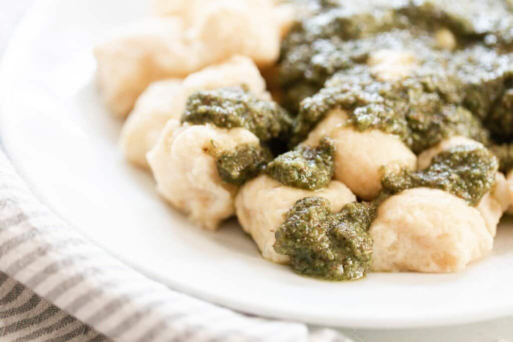homemade gnocchi topped with pesto on a white plate