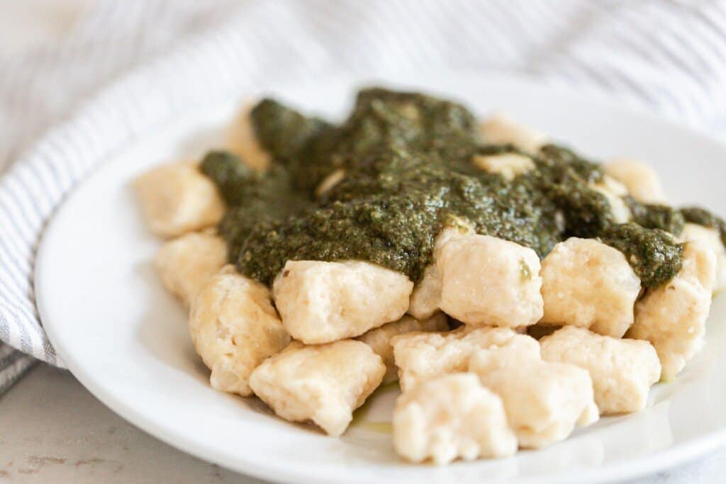 homemade pesto poured on top of gnocchi on a white plate.