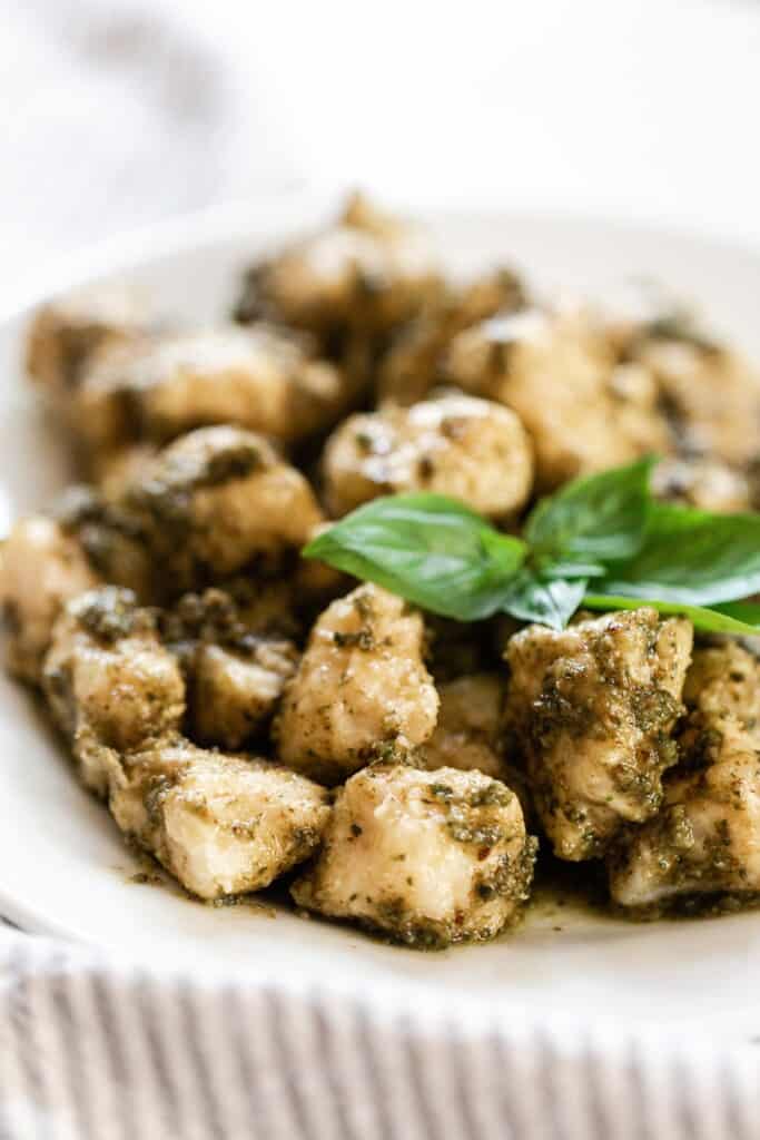 close up photo of homemade pesto gnocchi topped with fresh basil leaves on a white plate