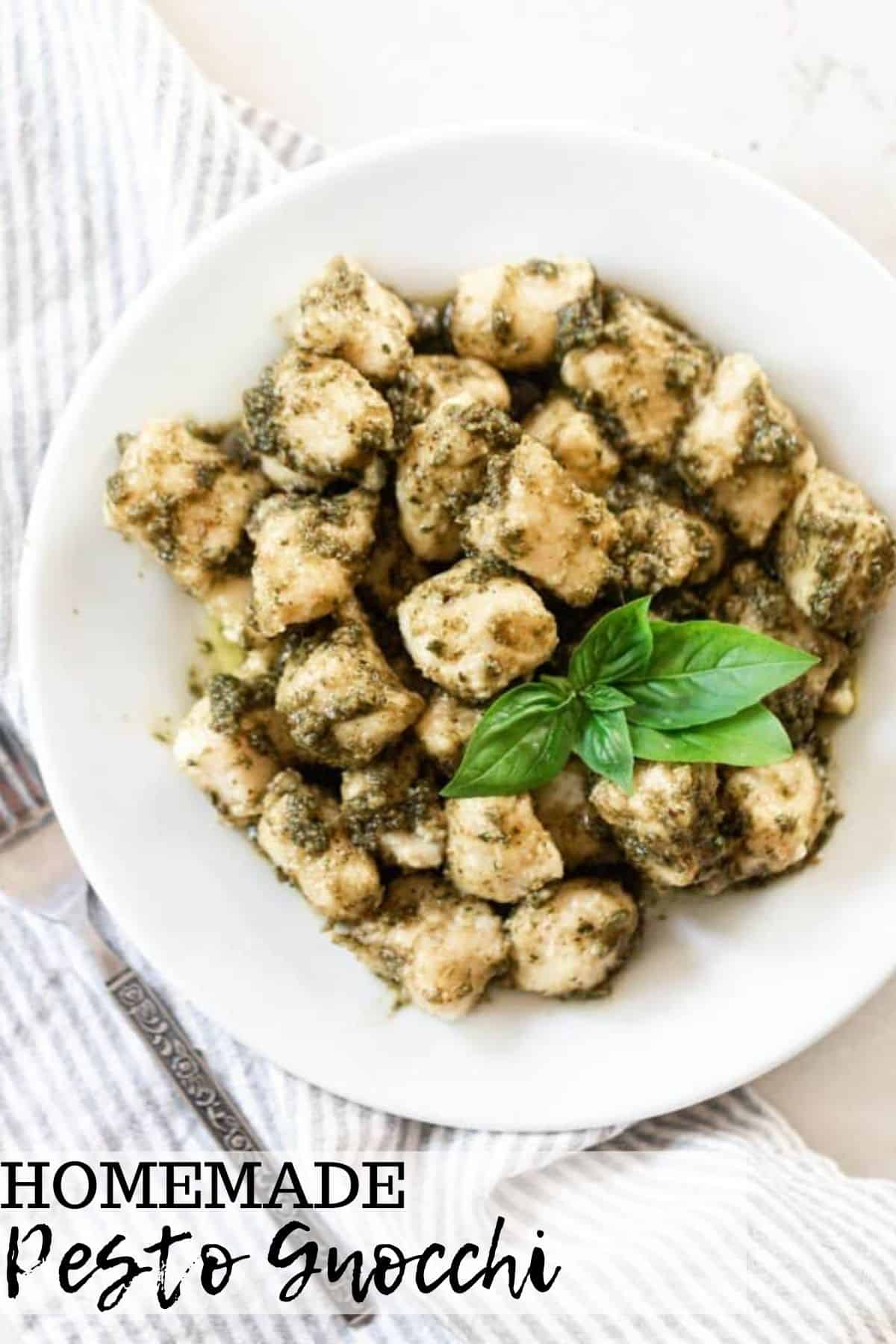 homemade gnocchi tossed in a fresh basil pesto and garnished with fresh basil leaves on a white plate with a blue ad white stripped napkin to the left