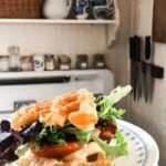 close up picture of a BLT made with sourdough cheddar waffles as the bread. The sandwich is on a white plate