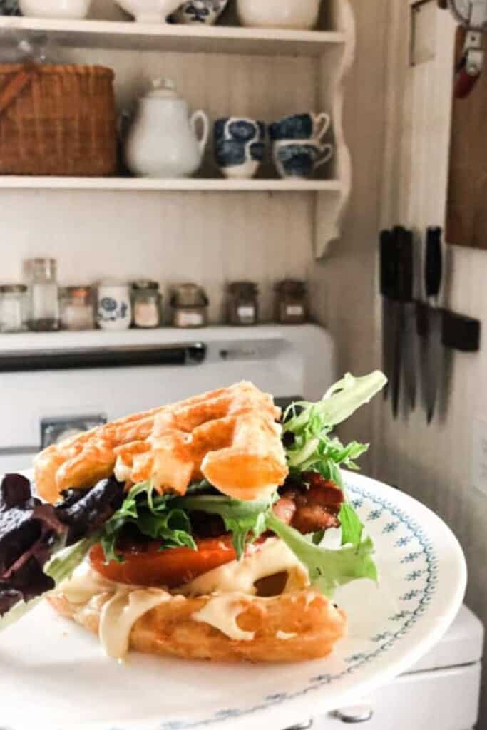 close up picture of a BLT made with sourdough cheddar waffles as the bread. The sandwich is on a white plate