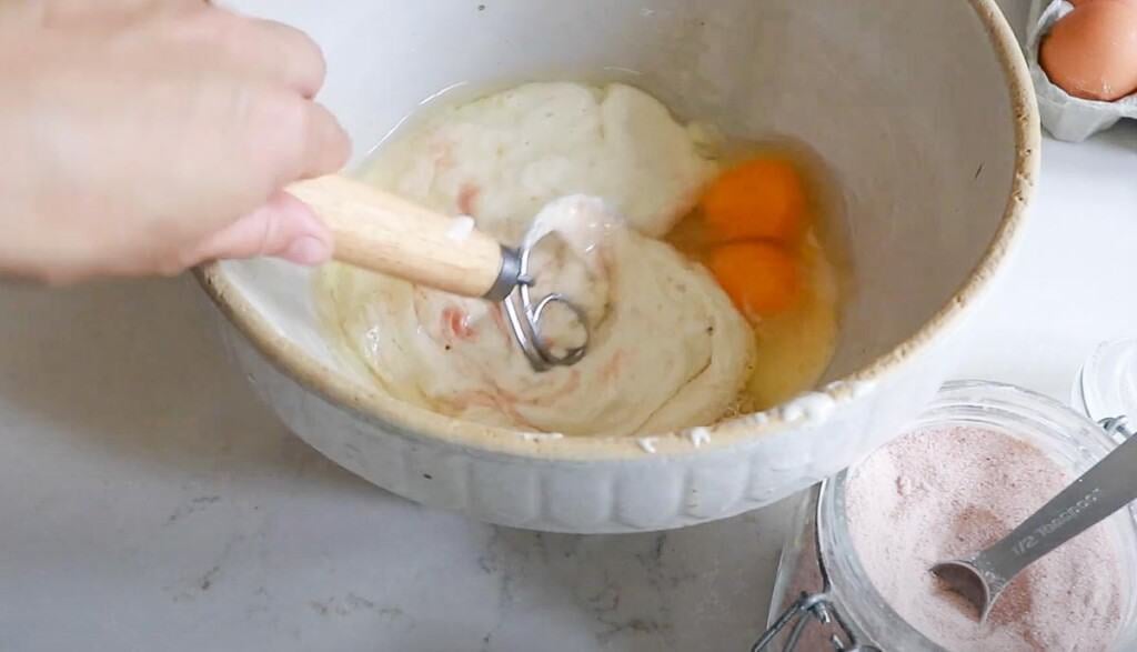 eggs, sourdough starter, and salt being mixed together with a dough whisk.