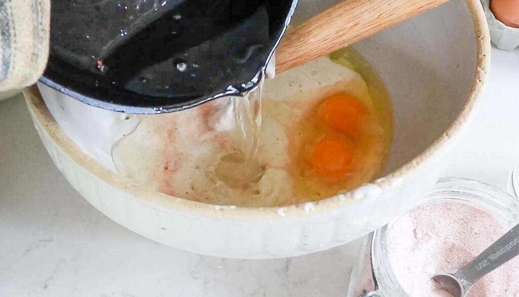 melted coconut oil in a cast iron skillet, being poured into a large bowl with eggs, salt, and sourdough starter